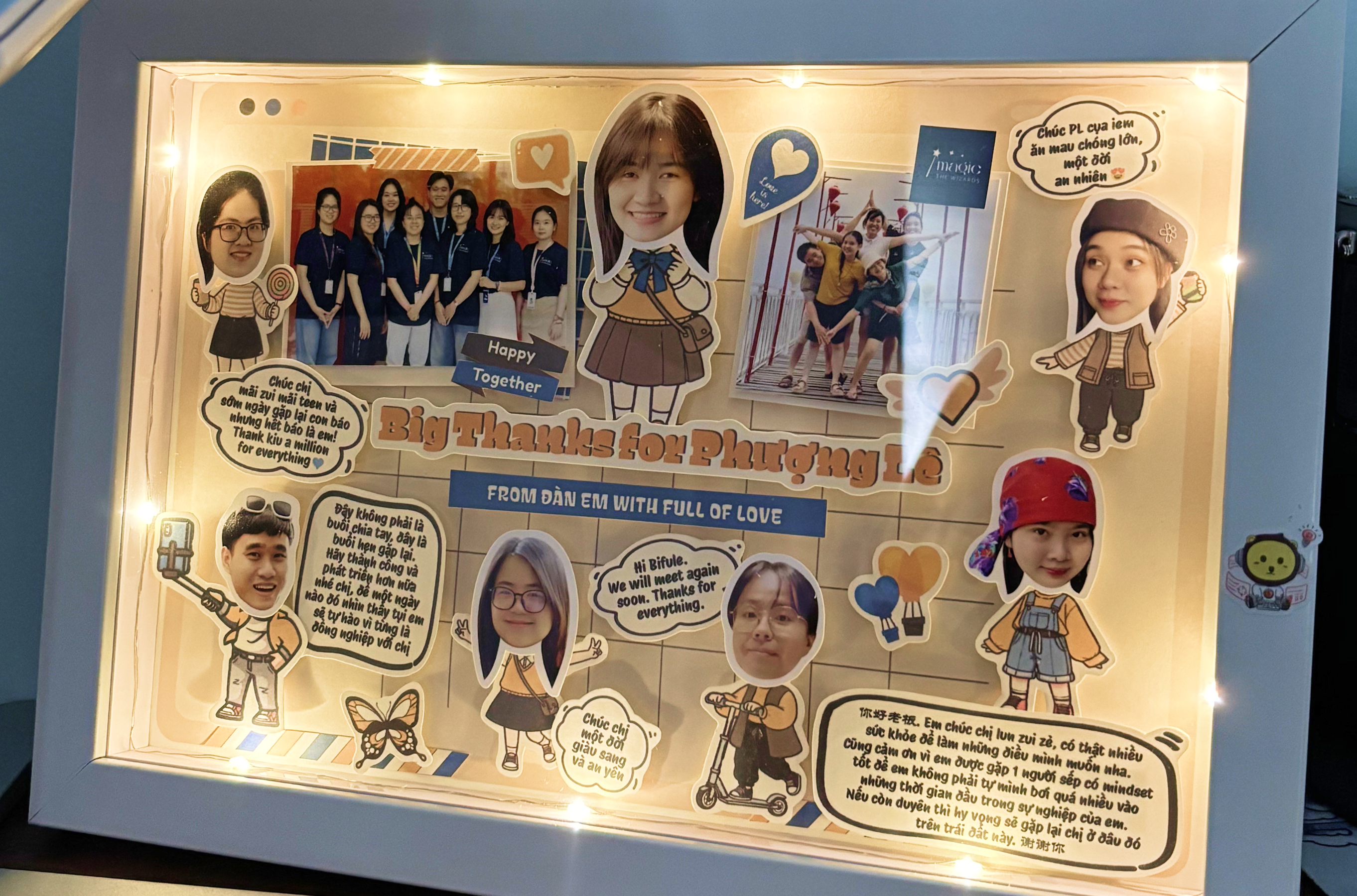 A framed, backlit photo collage of the team, decorated with cartoon cutouts and handwritten notes